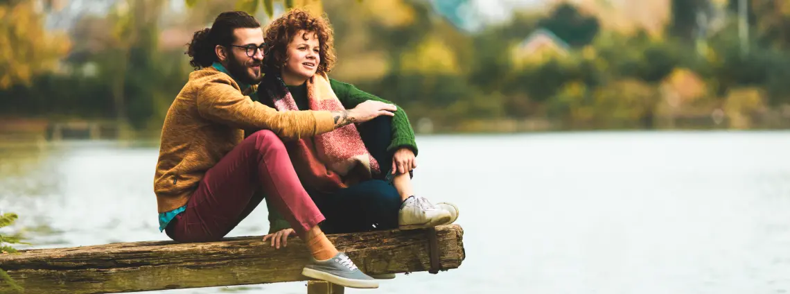 Nachhaltigkeit: Mann und Frau sitzen gemeinsam auf einem Steg und blicken auf einen See.