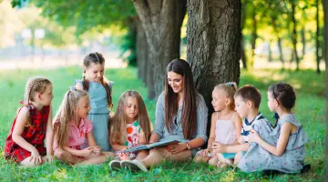 Schüler sitzen mit ihrer Lehrerin in der Natur unter einem Baum und lernen