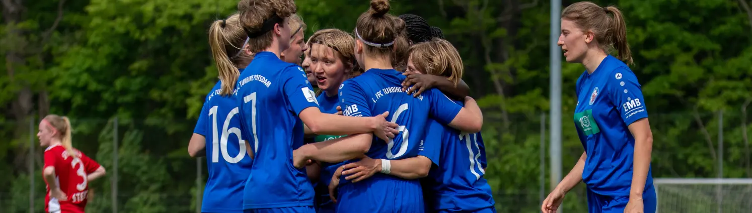 Fußballerinnen des U17 Teams des 1. FFC Turbine Potsdam im blauen Vereinstrikot umarmen sich auf dem Spielfeld.