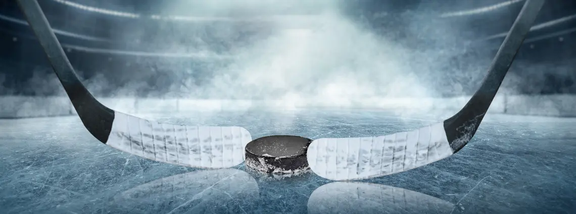 Zwei Eishockeyschläger und ein Puck liegen auf einer Eisfläche in einer großen Halle