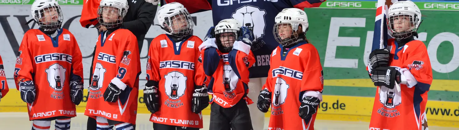 Mannschaft der Eisbären Juniors posiert in einer Reihe mit dem Eisbären-Maskottchen.