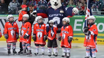 Mannschaft der Eisbären Juniors posiert in einer Reihe mit dem Eisbären-Maskottchen.