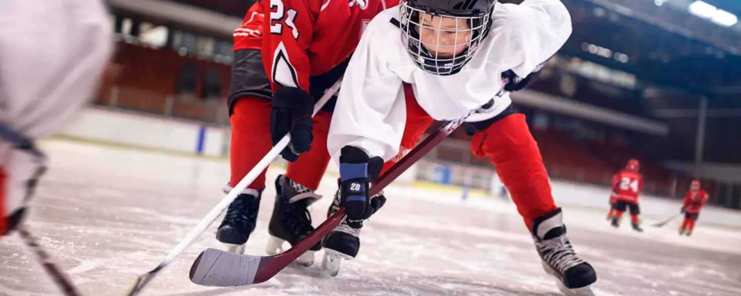 Zwei junge Eishockey-Spieler rangeln auf dem Spielfeld um den Puck.