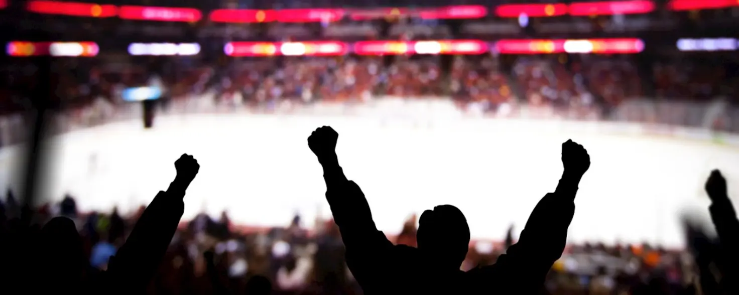 Dunkle Silhouetten von Fans jubeln in die Luft in einem Eishockey-Stadion.