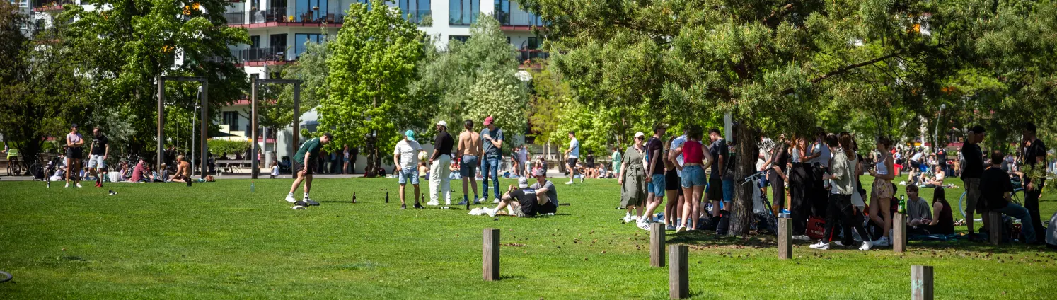 Eine bunte Gruppe von Menschen entspannt im grünen Park am Gleisdreieck in Berlin.