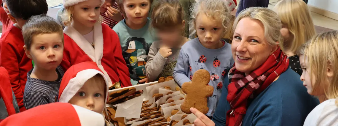 Frau verteilt Lebkuchen-Männchen und Kinder tragen Nikolaushüte