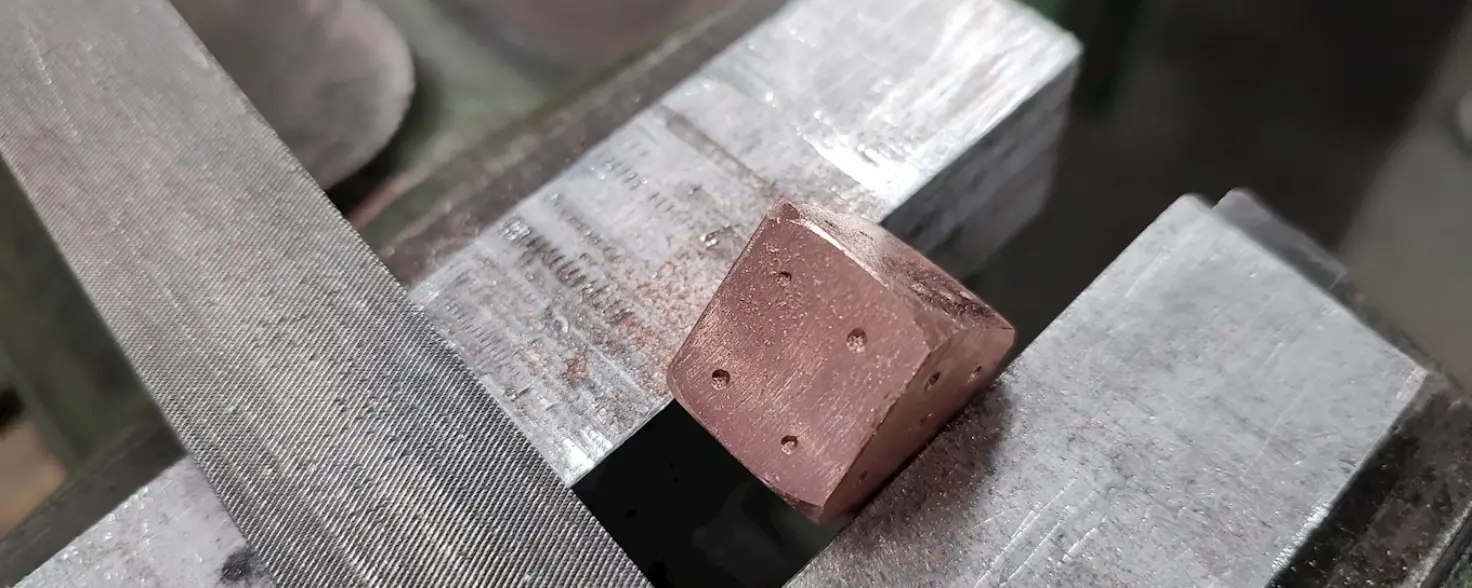 Ein kupferfarbener Metall-Würfel steck in einem Schraubstock