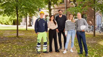 Fünf GASAG-Mitarbeiter in ihrer Arbeitskleidung stehen unter Bäumen vor einem Backsteingebäude