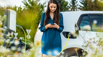 Eine Frau im blauen Kleid steht vor einem weißen E-Auto, das gerade lädt