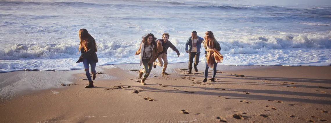 Eine Gruppe von Menschen tobt lachend am Meeresstrand.