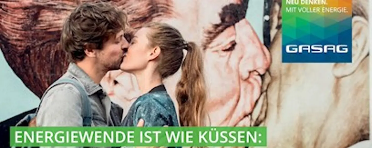 Ein Paar küsst sich vor der Berliner Mauer, auf dem der Bruderkuss zu sehen ist.