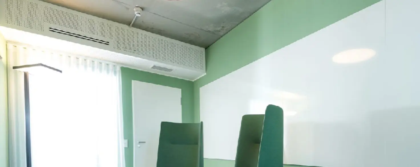 Zwei Sessel und ein kleiner Tisch stehen in einem Besprechungsraum vor einer grünen Wand