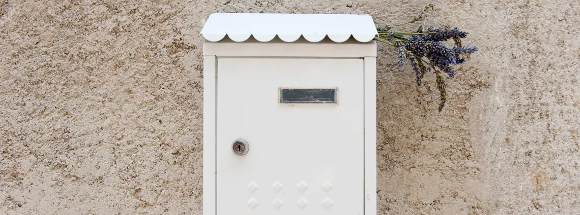 Ein weißer Briefkasten hängt an einer Hauswand mit Lavendelzweigen im Schlitz