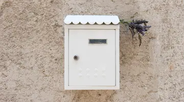 Ein weißer Briefkasten hängt an einer Hauswand mit Lavendelzweigen im Schlitz