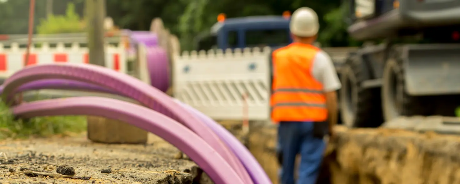 Breitbandausbau: Neues Glasfaserkabel wird in einem Graben verlegt. Im Hintergrund ein Bagger.