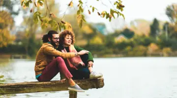 Nachhaltigkeit: Mann und Frau sitzen gemeinsam auf einem Steg und blicken auf einen See.