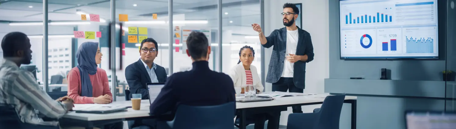 Mitarbeiter stellt seinem Team in einem Konferenzraum den aktuellen digitalen Geschäftsbericht vor.